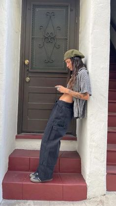 a woman leaning against a door looking at her cell phone while standing on the steps