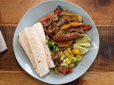 a white plate topped with meat and veggies next to a tortilla