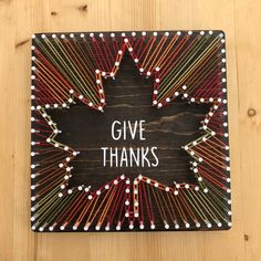 a wooden sign with the words give thanks written on it and colorful pins arranged in a star