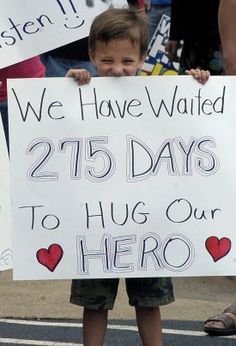 a young boy holding up a sign that says we have waited twenty days to hug our hero