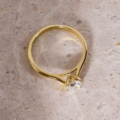 a yellow gold ring with a single diamond on top of it, sitting on a marble surface