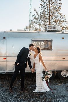 a bride and groom kissing in front of an airstream