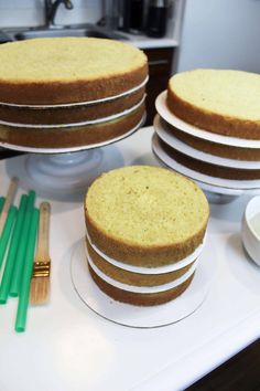 three cakes sitting on top of a white counter next to green plastic utensils