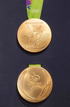 two gold medals with green ribbons around them on a black surface, one has the olympic logo