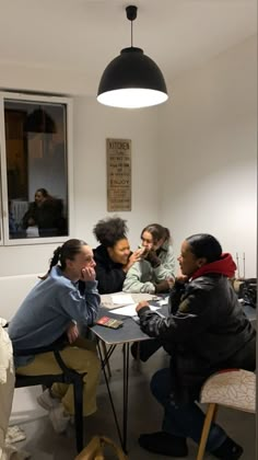 four people sitting at a table talking to each other in a room with white walls