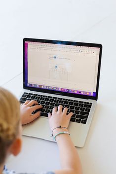 a woman sitting in front of a laptop computer on top of a white countertop