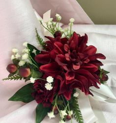 a bouquet of red flowers and greenery on a white cloth covered bed sheet,