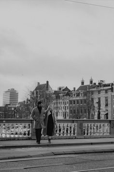 black and white photograph of two people walking across a bridge in the middle of town