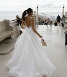 a woman in a white wedding dress walking towards the ocean