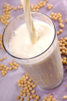 a glass filled with milk being poured into some kind of cereals on the table