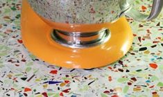 an orange stand mixer sitting on top of a colorful table cloth covered flooring with multicolored tiles