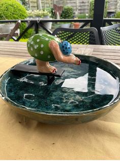 a ceramic figurine is sitting on top of a glass bowl that has been placed on a table