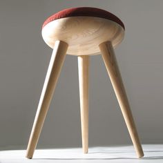 a wooden stool with a red cushion sitting on it's back legs in front of a white wall