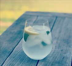 a glass filled with ice and lemon on top of a wooden table