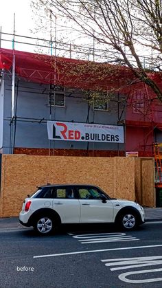 a white car parked in front of a building under construction with a red sign on it