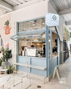 an open air cafe with blue walls and white furniture in the front, surrounded by greenery