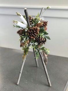 a bouquet of pine cones and greenery on top of a metal table with white feathers