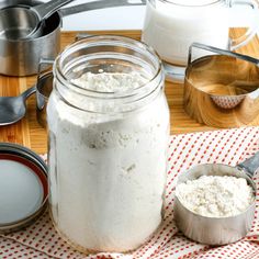 a glass jar filled with white powder next to measuring spoons on a wooden table