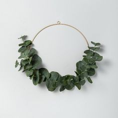 a wreath made out of green leaves on a white wall with a string hanging from it