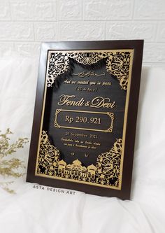 a black and gold wedding card with an ornate design on the front, in wood frame