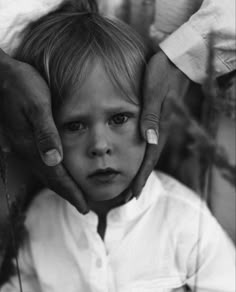 a black and white photo of a young boy being held by an adult's hands