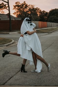 two women in white dresses and black stockings are walking down the street with their arms around each other