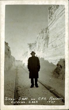 an old photo of a man standing in the middle of train tracks near a mountain