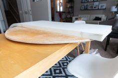 a surfboard sitting on top of a wooden table next to a white plastic chair