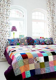 a bed with colorful quilts and pillows on top of it in a room next to a window