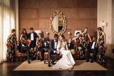 a large group of people in formal wear posing for a wedding photo with a mirror on the wall behind them