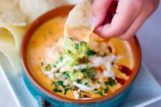 a person dipping tortilla chips into a bowl of soup