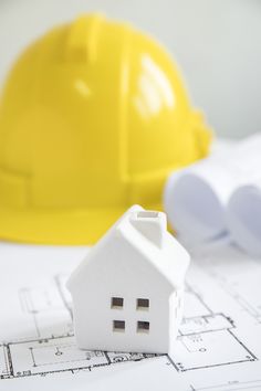 a house model sitting on top of blueprints next to a yellow hard hat