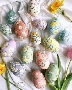 an arrangement of painted eggs and flowers on a white table cloth with twine string