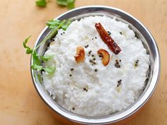 a bowl filled with rice and nuts on top of a wooden table next to a spoon