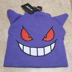 a purple beanie with red eyes and fangs on the front is laying on a tile floor