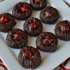 chocolate covered cookies with cherries are on a white plate and red tablecloths