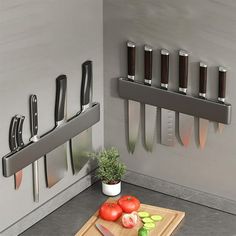 a cutting board with knifes and tomatoes on it next to knives hanging from the wall