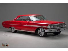 an old red car is parked in a room with gray walls and white flooring