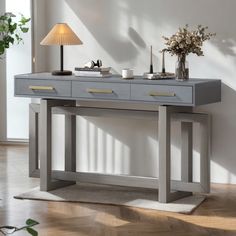 a grey table with two drawers and a lamp on the side, in front of a white wall