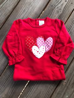 a red shirt with hearts on it sitting on a wooden floor next to a string