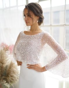 a woman standing in front of a window wearing a white dress with sequins on it