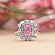 a pink and white diamond ring sitting on top of a table next to some flowers