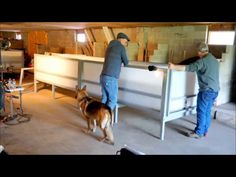 two men are working on some furniture in an unfinished room with a dog standing next to them