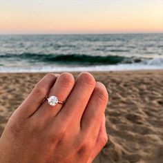 a person holding a diamond ring in their hand on the beach with waves coming in