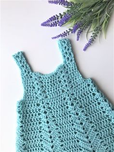 a blue crocheted dress next to purple flowers