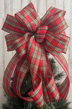 a red and green plaid bow on top of a christmas tree in front of a white wooden wall