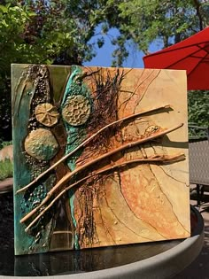 an abstract painting is displayed on top of a table outside with umbrellas in the background