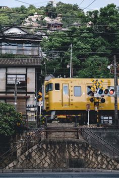 a yellow train traveling down tracks next to a lush green hillside covered in trees and buildings