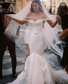 a woman in a white wedding dress is walking down the street with her veil over her head