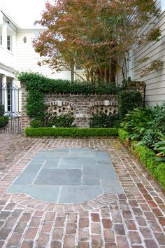 an outdoor courtyard with brick pavers and green plants on the side of the house